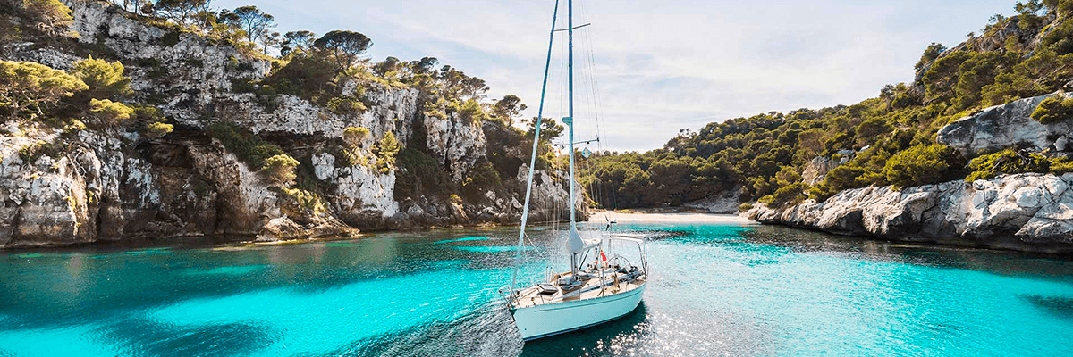 Velero navegando en cala de Menorca con aguas turquesas, grupo de singles.