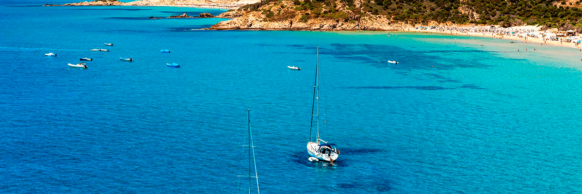 Velero navegando en aguas turquesas de Mallorca con un grupo de amigos singles a bordo, vistas de calas y acantilados.
