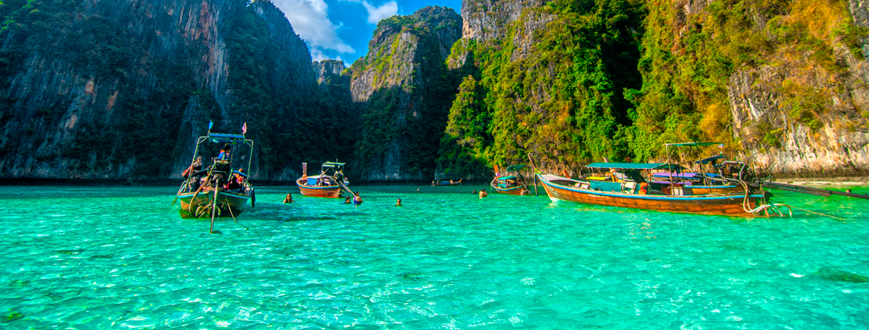 Barcas tradicionales navegando en una bahía de aguas turquesas y acantilados tropicales, representando la experiencia de Malasia, selva y playas en grupo.